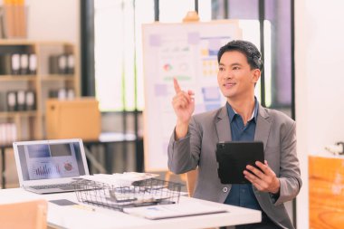 Genç Asyalı işadamı, bilgisayarla çalışırken gülümsüyor ve iş hayatında başarılı olma kavramına sahip.