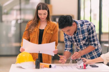 Mimarlar ve mühendisler inşaat projesi baskı kağıtlarını inceliyor. İnşaat yöneticisi proje sahibiyle ofisteki yapısal materyaller hakkında konuşur..
