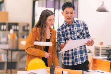 Mimarlar ve mühendisler inşaat projesi baskı kağıtlarını inceliyor. İnşaat yöneticisi proje sahibiyle ofisteki yapısal materyaller hakkında konuşur..