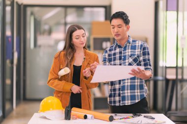 Mimarlar ve mühendisler inşaat projesi baskı kağıtlarını inceliyor. İnşaat yöneticisi proje sahibiyle ofisteki yapısal materyaller hakkında konuşur..