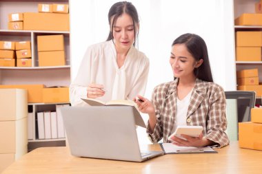 İki Asyalı KOBİ işletmesi sahibi, iki kadın mağaza sahibinin mutlu yüzleri var. Müşterilerin siparişlerini kontrol ediyorlar. Malları nakliye şirketi aracılığıyla getiriyorlar..