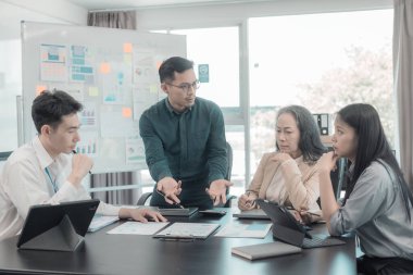 İş sunumu ya da seminer için Asyalı iş adamları konferans odasında. Belgelerde mali ya da pazarlama rakamları, grafikleri ve grafikleri var. Şirket hisselerini analiz etmek için bir laptop var..