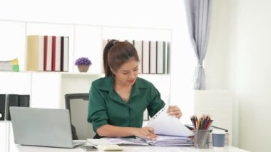 Diz üstü bilgisayarı kullanarak vergi, muhasebe, istatistik ve analiz araştırması yapan Asyalı iş kadını ve masada hesap makinesi ile birlikte belgeler, planlama ve mali raporları analiz ediyor..