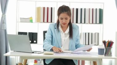 Diz üstü bilgisayarı kullanarak vergi, muhasebe, istatistik ve analiz araştırması yapan Asyalı iş kadını ve masada hesap makinesi ile birlikte belgeler, planlama ve mali raporları analiz ediyor..