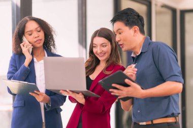 Bir grup genç iş adamı, farklı uluslardan yeni iş adamları modern ofiste buluşup beyin fırtınası yapıyorlar, dizüstü bilgisayarlar ve tabletler üzerinde çalışıyorlar ve finansal tablolar hazırlıyorlar..