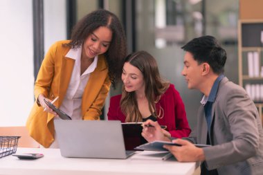 Bir grup genç iş adamı, farklı uluslardan yeni iş adamları modern ofiste buluşup beyin fırtınası yapıyorlar, dizüstü bilgisayarlar ve tabletler üzerinde çalışıyorlar ve finansal tablolar hazırlıyorlar..