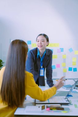 Bir grup iş kadını başarılı takım çalışmalarının sonuçlarını gösteren çizelge ve grafikleri tartışıyor. Asyalı iş kadınları yaratıcı ofis alanlarında iş arkadaşlarıyla beyin fırtınası yapıyorlar. Dikey resimleme.