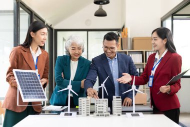 Rüzgar türbini modeli ve ev modeli için mühendisler buluşuyor. Yenilenebilir enerji ve konut geliştirme kavramı. Modern ofiste mimarlardan ve mühendislerden oluşan bir ekip tasarım yapısını tartışıyor..