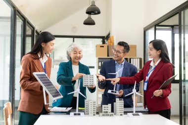 Rüzgar türbini modeli ve ev modeli için mühendisler buluşuyor. Yenilenebilir enerji ve konut geliştirme kavramı. Modern ofiste mimarlardan ve mühendislerden oluşan bir ekip tasarım yapısını tartışıyor..