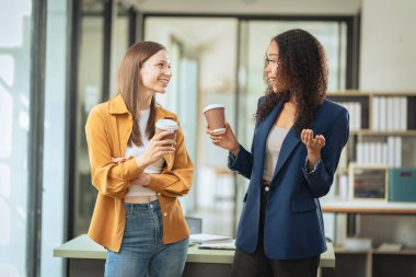 İki bayan meslektaşın dizüstü bilgisayarlarla şirket işlerini tartışıyor ve vurgulu ifadeleri önemli iş konularını tartıştıklarını gösteriyor..