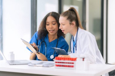 İki kadın bilimadamı, kan örnekleri ve test tüpleriyle bir laboratuvarda çalışıyorlar. Araştırmalarını sürdürürken, çözeltileri damlalardan gelen pipetlerle dolduruyorlar..