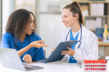 İki kadın bilimadamı, kan örnekleri ve test tüpleriyle bir laboratuvarda çalışıyorlar. Araştırmalarını sürdürürken, çözeltileri damlalardan gelen pipetlerle dolduruyorlar..