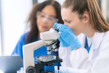 Koruyucu gözlüklü iki kadın tıp bilimcisi ve araştırma yaparken bir damlacıktan gelen bir pipetle çözelti dolu bir test tüpü..