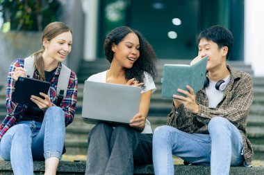 Çok ırklı üniversite öğrencileri dizüstü bilgisayarlar üzerine kitaplar okuyor, sınavlara hazırlanıyor ya da kampüste grup çalışması yapıyor, modern araçları eğitim için kullanıyor..