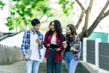 Çok ırklı üniversite öğrencileri dizüstü bilgisayarlar üzerine kitaplar okuyor, sınavlara hazırlanıyor ya da kampüste grup çalışması yapıyor, modern araçları eğitim için kullanıyor..