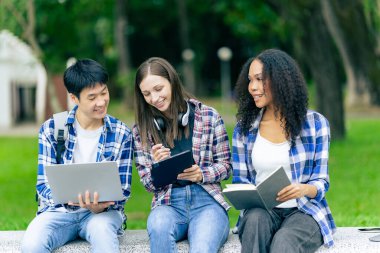 Çok ırklı üniversite öğrencileri dizüstü bilgisayarlar üzerine kitaplar okuyor, sınavlara hazırlanıyor ya da kampüste grup çalışması yapıyor, modern araçları eğitim için kullanıyor..