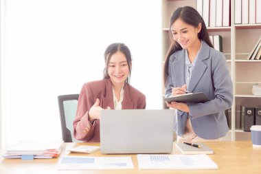 İki Asyalı kadın, mali grafik belgeleriyle çalışmak için hesap makinesi kullanarak kazanç ve iş gücünü artırmak için iş fikirlerini değiştirmek için konuşuyor..