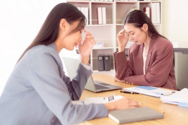 Asyalı kadın iki elini alnına bastırıyor. Stresli hissediyor. Belgeler ve dizüstü bilgisayarla kötü finansal işlerden endişe ediyor.