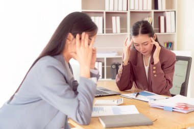 Asyalı kadın iki elini alnına bastırıyor. Stresli hissediyor. Belgeler ve dizüstü bilgisayarla kötü finansal işlerden endişe ediyor.