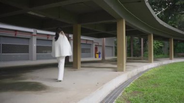 Beyaz takım elbiseli bir tablet taşıyan Asyalı iş kadını kendinden emin ve günlük kıyafetlerle bağımsızdır. Gündüz vakti gülümseyen ve yürüyen - yavaş çekim