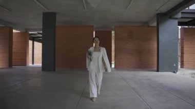 Beyaz takım elbiseli bir tablet taşıyan Asyalı iş kadını kendinden emin ve günlük kıyafetlerle bağımsızdır. Gündüz vakti gülümseyen ve yürüyen - yavaş çekim