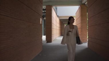 Beyaz takım elbiseli bir tablet taşıyan Asyalı iş kadını kendinden emin ve günlük kıyafetlerle bağımsızdır. Gündüz vakti gülümseyen ve yürüyen - yavaş çekim