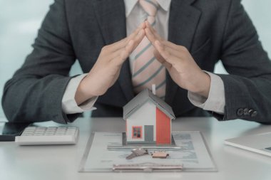 Erkek işadamının elleri ahşap bir ev sigortası ve güvenlik konseptini kapsıyor. Evrak ve dizüstü bilgisayarı olan bir ev modelinin yakın çekimi. dikey yakın plan resim