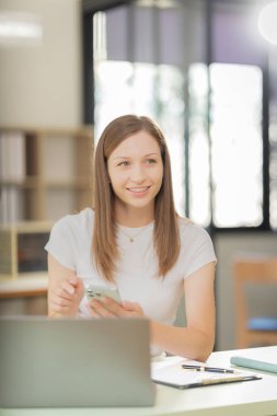 Finansal tabletlerle çevrili bir bilgisayarla çalışan kadın finans analisti, evdeki masada dijital tablet kullanıyor ve veri belgelerini analiz ediyor.