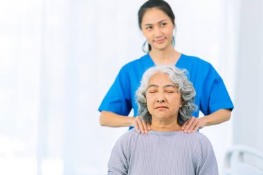 Yaşlı bir Asyalı kadın hasta mutlu ve gülümsüyor, onu yürümesi için fiziksel terapi yapmaya teşvik ediyor ve destekliyor. Sağlık hizmeti kavramı