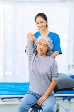 Yaşlı bir Asyalı kadın hasta mutlu ve gülümsüyor, onu yürümesi için fiziksel terapi yapmaya teşvik ediyor ve destekliyor. Sağlık hizmeti kavramı