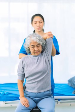 Yaşlı bir Asyalı kadın hasta mutlu ve gülümsüyor, onu yürümesi için fiziksel terapi yapmaya teşvik ediyor ve destekliyor. Sağlık hizmeti kavramı