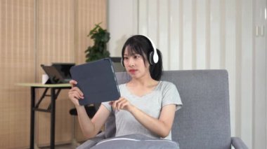Kanepede tablet kullanan Asyalı kadın internet sörf ekranında yazılan metne bakın. Sosyal medya, çevrimiçi alışveriş teknolojisi kavramı