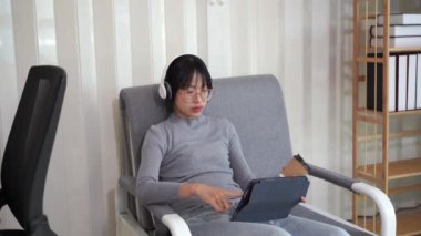 Kanepede tablet kullanan Asyalı kadın internet sörf ekranında yazılan metne bakın. Sosyal medya, çevrimiçi alışveriş teknolojisi kavramı