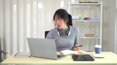 Kulaklık takan genç Asyalı bir kız evdeki sosyal karantinada dijital bir dizüstü bilgisayarla çevrimiçi müfredat geliştirme programı dinliyor. Sınıfta becerilerin artmasına yardımcı olur