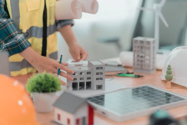 Çok ırklı bir grup erkek ve kadın mimar ve müteahhit bir ofis masasının etrafında durmuş planlara ve masanın üzerindeki ev planlarına bakıyorlar. Yakın plan fotoğraf.