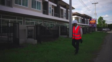 Yapısal teftiş tabletiyle inşaat projesini denetleyen erkek mühendis yolda yürürken kask takın. Yavaş çekim videosu