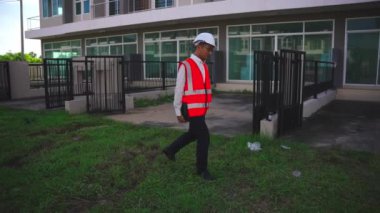 Yapısal teftiş tabletiyle inşaat projesini denetleyen erkek mühendis yolda yürürken kask takın. Yavaş çekim videosu