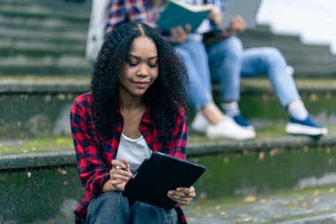 Çeşitli genç üniversite öğrencileri dışarıda dizüstü bilgisayar ve tabletlerle çalışarak teknoloji öğrenme kavramlarını tartışıyor..