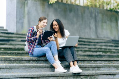 Çeşitli genç üniversite öğrencileri dışarıda dizüstü bilgisayar ve tabletlerle çalışarak teknoloji öğrenme kavramlarını tartışıyor..