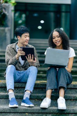 Çeşitli genç üniversite öğrencileri dışarıda dizüstü bilgisayar ve tabletlerle çalışarak teknoloji öğrenme kavramlarını tartışıyor..