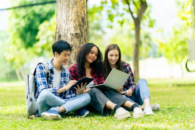 Çeşitli genç üniversite öğrencileri dışarıda dizüstü bilgisayar ve tabletlerle çalışarak teknoloji öğrenme kavramlarını tartışıyor..