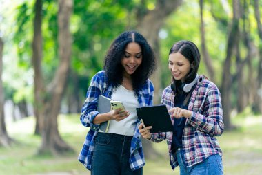 Çeşitli genç üniversite öğrencileri dışarıda dizüstü bilgisayar ve tabletlerle çalışarak teknoloji öğrenme kavramlarını tartışıyor..