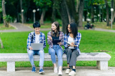Çeşitli genç üniversite öğrencileri dışarıda dizüstü bilgisayar ve tabletlerle çalışarak teknoloji öğrenme kavramlarını tartışıyor..