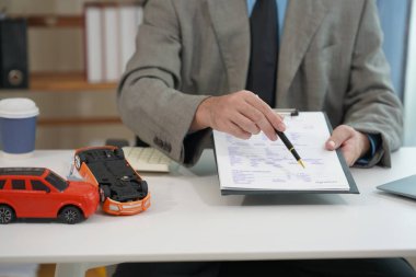 Araba sigortası ve finansal planlama konseptleri. Küçük oyuncak araba modeli. Araba sigortası belgelerinin yanına yerleştirilmiş. İşadamı kalem ve hesap makinesini ahşap masa üzerinde tutuyor.