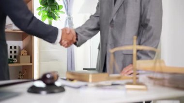 Ofiste iki avukat el sıkışıyor. Hukuki belgeler, masanın üzerinde çekiç, hukuki tavsiyeler, işlemler, iş birliği toplantılarından mahkeme salonunda iyi anlaşmalara kadar..