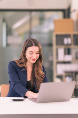 Ofis internet teknolojisi şirketinde çalışmak için dizüstü bilgisayar kullanan başarılı bir iş kadını: Millennial kadın profesyonel çalışan iş yerinde dizüstü bilgisayarında e-posta yazıyor.