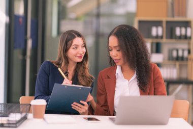 İki Asyalı iş kadını, şirketteki mali durumu tartışmak için dizüstü bilgisayarlarla bir araya gelip finansal tabloları analiz ediyorlar..