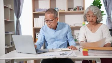Emekli Asyalı yaşlı çift mali belgelerle ilgili mali hesaplamalar yapıyor ve inceliyor. Bilgisayarla vergilerini öde
