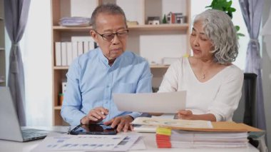 Emekli Asyalı yaşlı çift mali belgelerle ilgili mali hesaplamalar yapıyor ve inceliyor. Bilgisayarla vergilerini öde