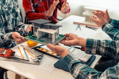 Yeni emlak projesinde çalışırken, mimarın dijital tablet tutarken, mühendislik aletleri ve mimari model ev, bina ve inşaatı ile masada otururken çekilmiş görüntüleri..